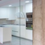 Cocina con pared de cristal y revestimiento madera en el salón